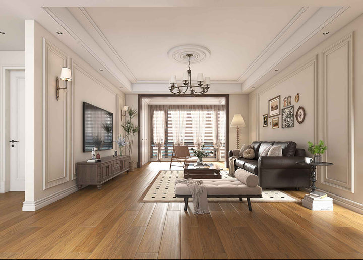A bright, modern living room with warm wood flooring, cream paneled walls, a dark leather sofa, a beige ottoman, and a wall-mounted television.