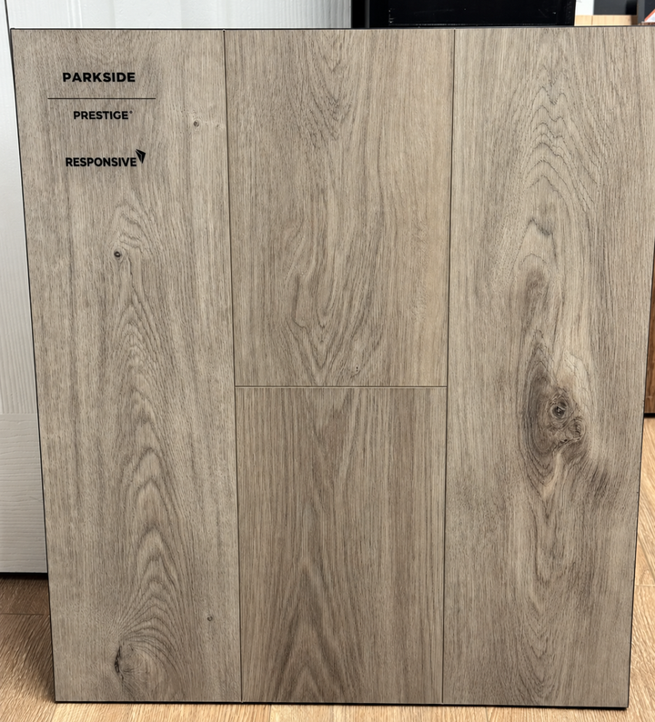 A large square sample of Parkside Prestige Responsive flooring shown in a light gray-brown woodgrain finish, standing upright indoors.