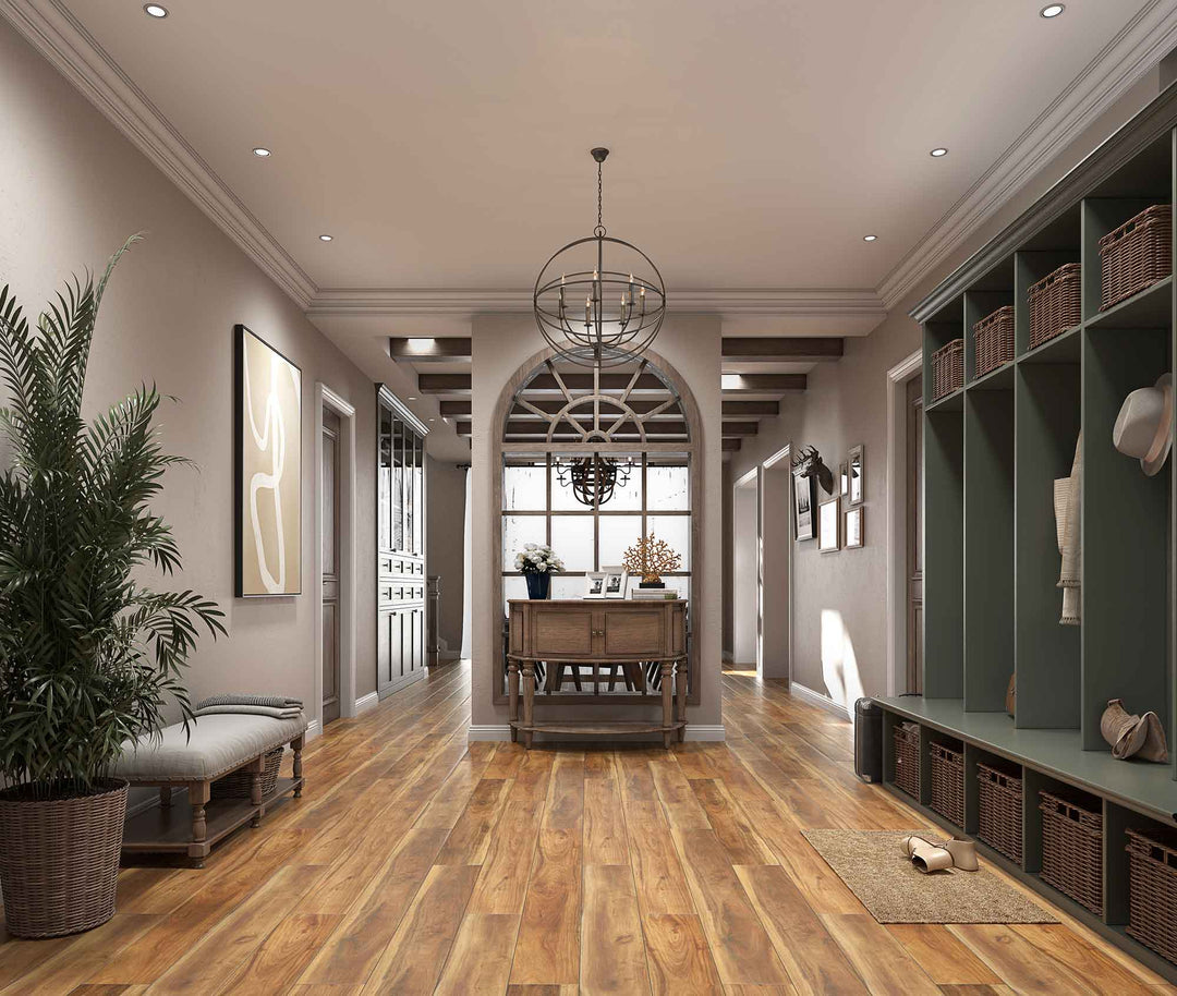 A wide, bright entryway with warm wood flooring, a long bench with a potted palm on the left, built-in green storage shelves with baskets on the right, and a chandelier hanging over a central table.