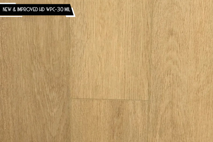 Light oak wood flooring planks with a warm beige-brown finish and visible grain texture, with a small black text banner in the top-left corner reading 'NEW & IMPROVED HD WPC-30 MIL'.